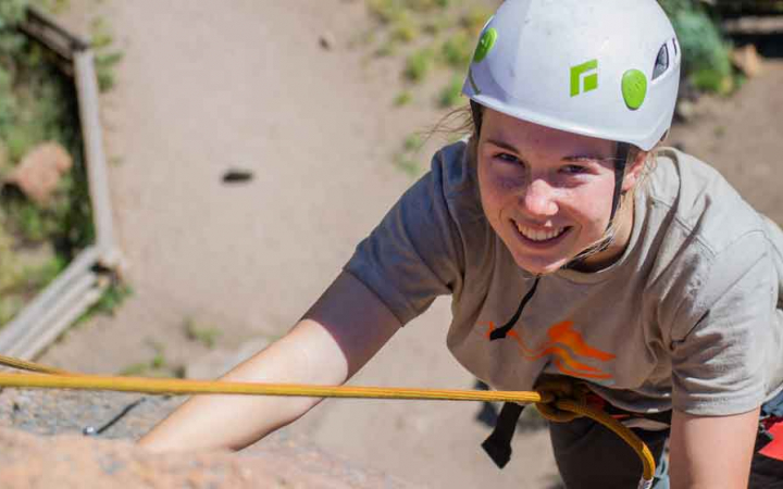 girls smiles while rock climbing on outward bound expedition 